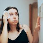 Woman checking thermostat settings while blotting sweat from forehead