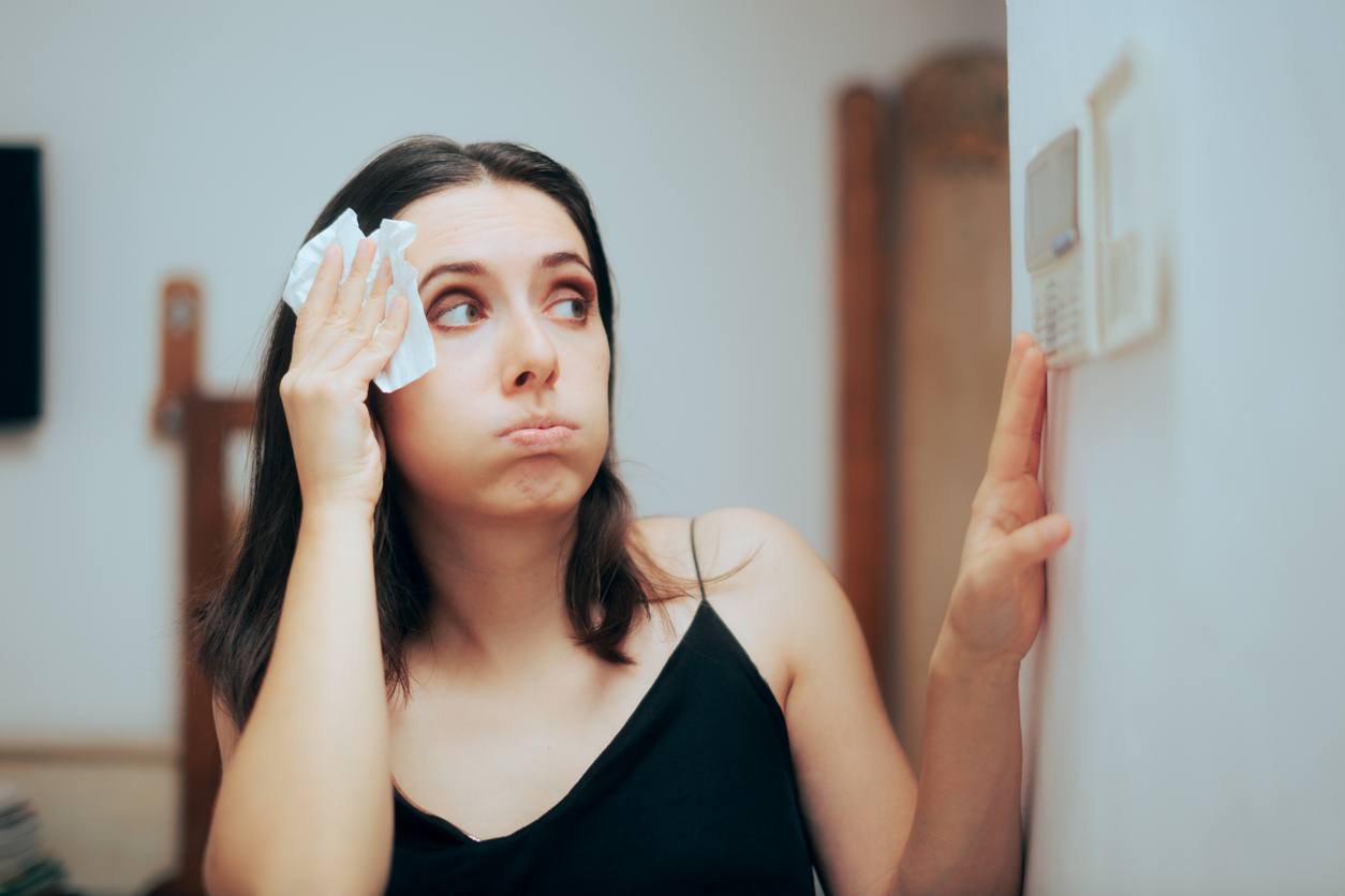 Woman checking thermostat settings while blotting sweat from forehead