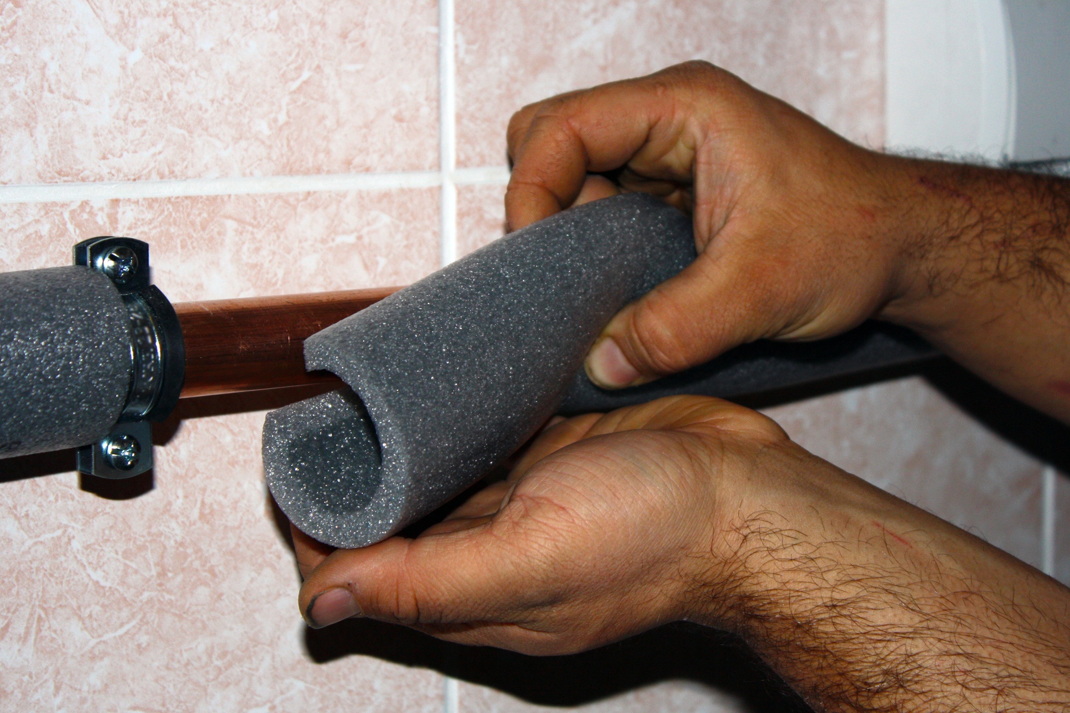 Close up of a man applying foam pipe insulation to an exposed pipe