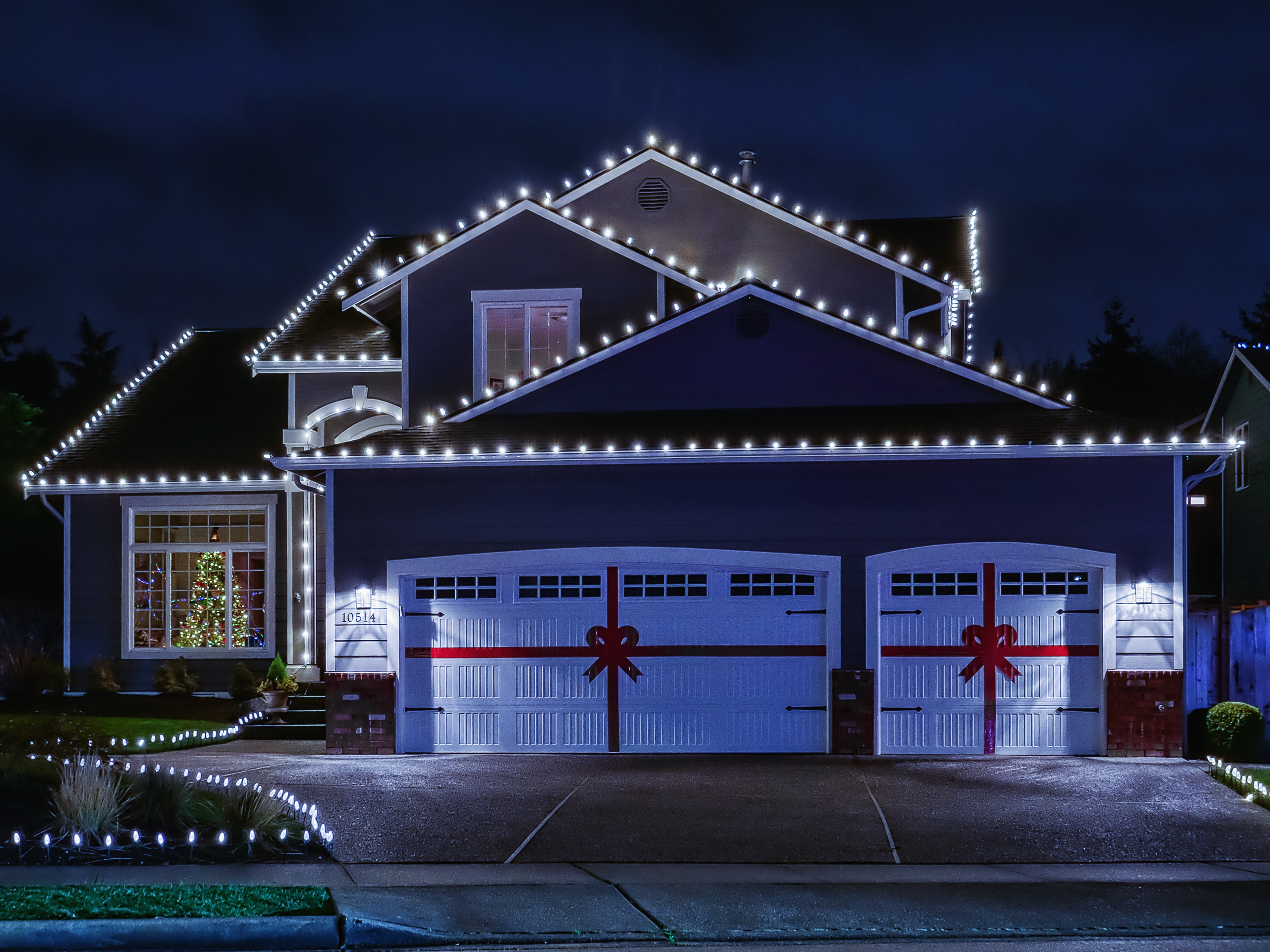 Night time photo of a modern American suburban home decorated with festive Christmas holiday lights and red ribbons on garage doors